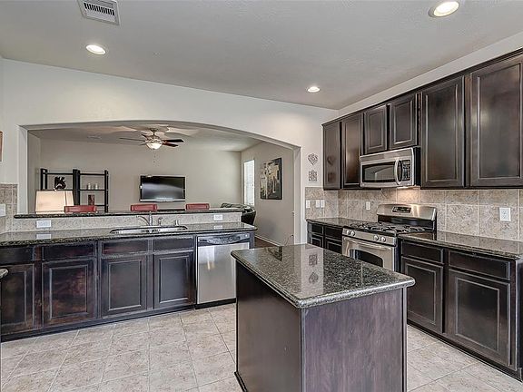 Open and light island kitchen with stainless steel appliances.