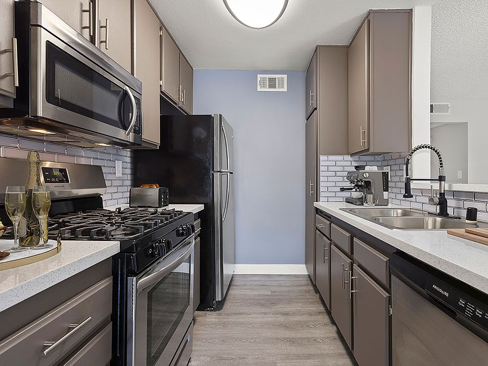 Tiled kitchen with stainless steel microwave, oven, and fridge.
