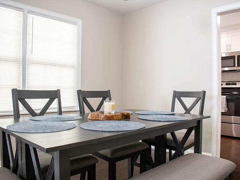 Dining area features a full-size table with seating for four, set beside large windows and open to the adjacent kitchen.