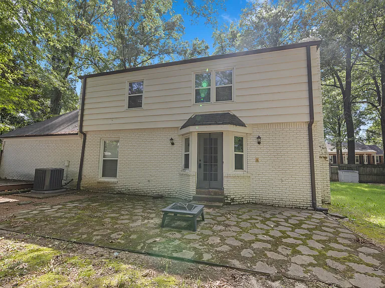 Charming back exterior with stone patio, French doors, and lush tree-lined yard _ your private outdoor escape.