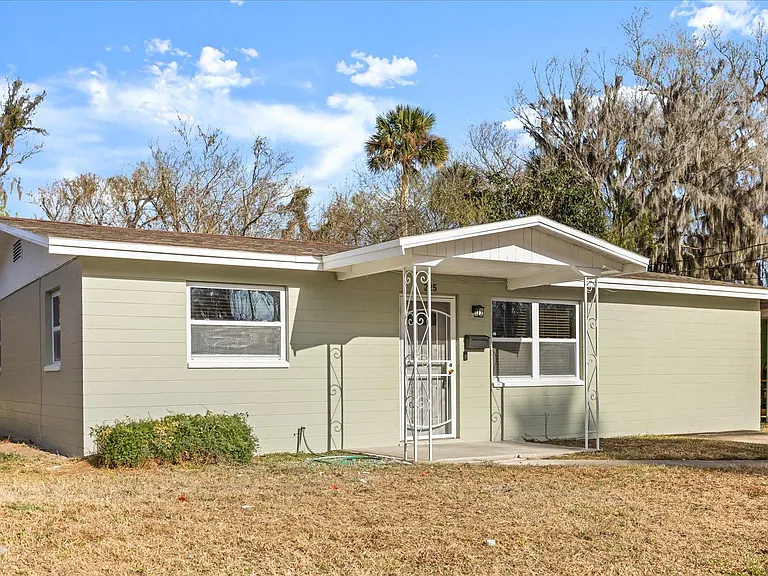 Single-story home with a covered front entry, large front windows, and an open yard with mature trees.