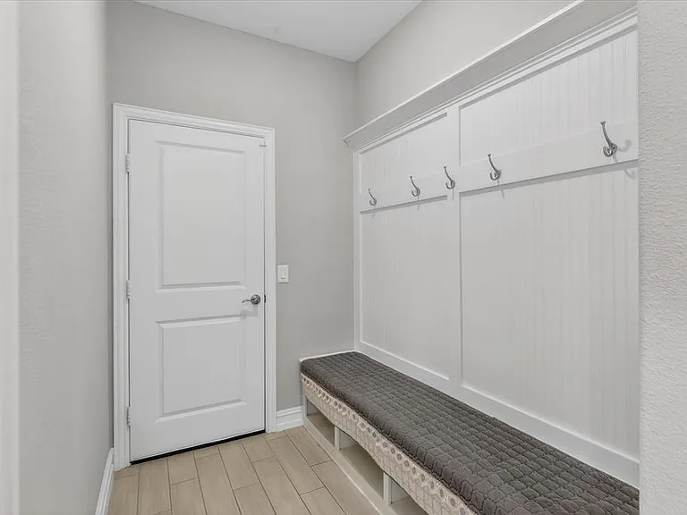 Entryway featuring built-in white beadboard paneling with integrated coat hooks and a storage bench