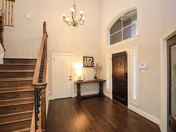 GRAND FOYER WITH RICH WOOD FLOORS AND RUSTIC 2-PANEL V-GROOVE SPEAKEASY EXTERIOR DOOR - A view of the entry with new solid hardwood flooring (throughout the first floor), stunning chandelier, side panel entry door windows with plantation shutters. Ju