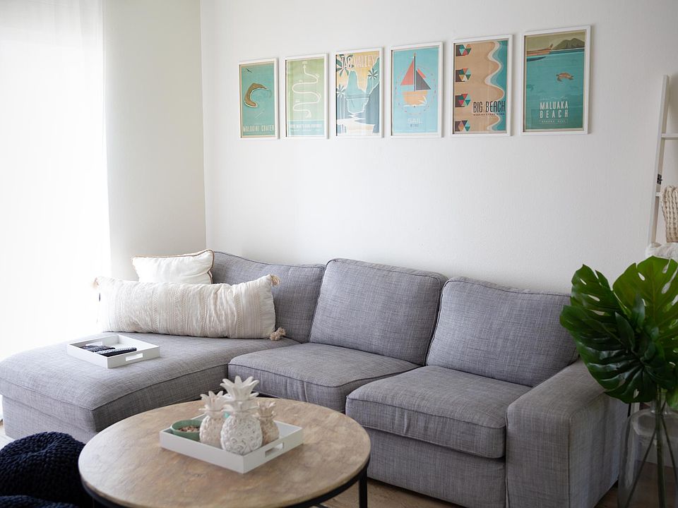 Opposite side of living room. Couch, wall art, coffee table, blanket ladder, and plant are included.