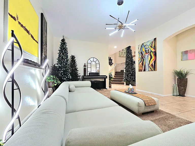 Spacious shared living area with sectional seating, statement lighting, and open sightlines to the entry and stairs.