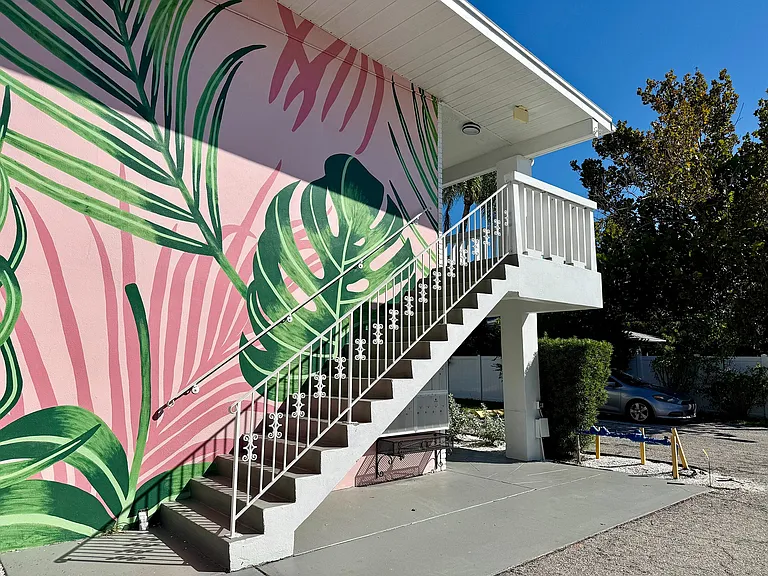 Vibrant apartment exterior with tropical leaf mural, elegant white staircase, and sunny surroundings.