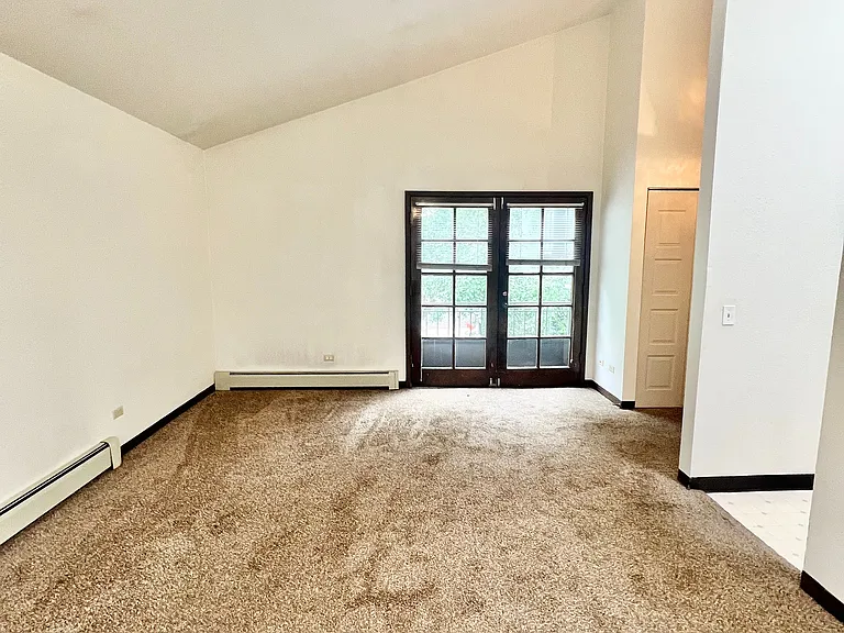 Bright and spacious living room with plush carpet and French doors leading to a serene outdoor view.