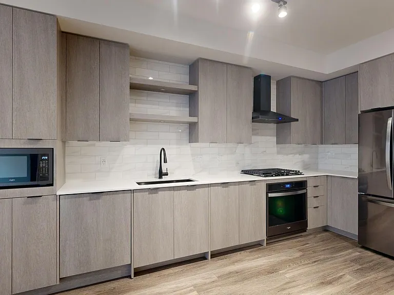 Apartment kitchen with black stainless steel appliances, quartz countertops, wood-style flooring, and custom Italian cabinetry.