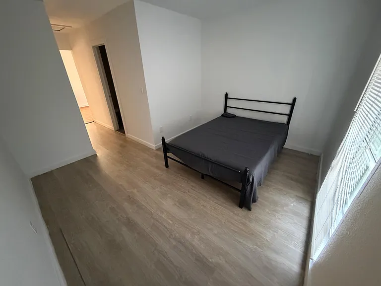 Private bedroom with wood-style flooring, a bed frame, and a window with blinds for natural light and privacy.