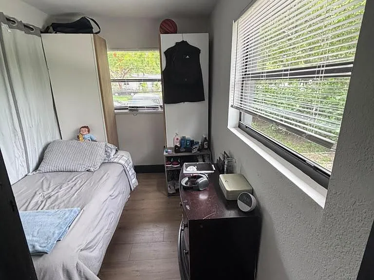 Efficient bedroom with wood-look flooring, a large window with blinds, and space for a bed plus dresser or desk.