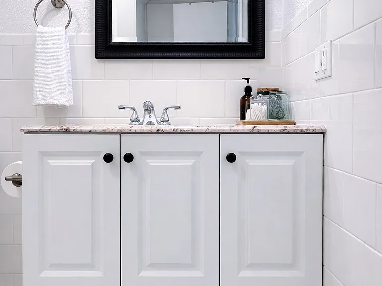 Clean, light-toned vanity with a marble countertop and ample storage, including a full wall cabinet behind the door.