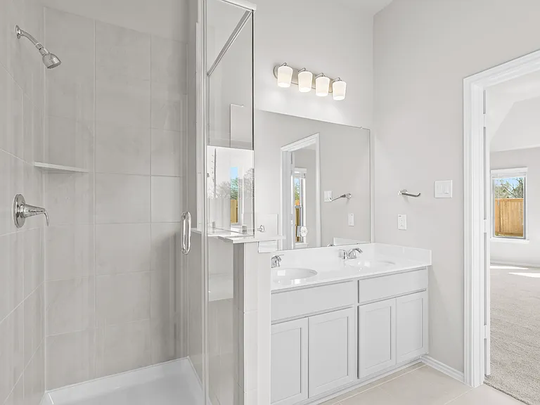 Primary bathroom featuring a glass-enclosed separate shower with tile surround and double vanity with quartz countertops.