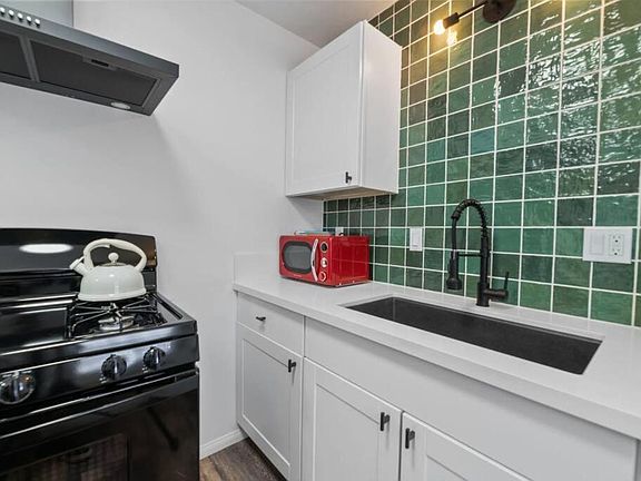 Updated kitchen featuring white shaker cabinetry, solid-surface counters, deep sink, and a gas range with hood.