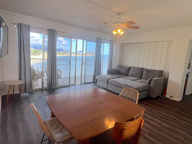 View of living room out to lanai with amazing ocean and mountain views! This photo shows doors shut to primary bedroom, and sofa opened up to bed/lounging option.