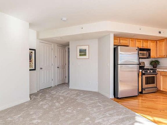 Carpeted living space with hardwood maple floors and kitchen cabinets. Stainless steel appliances.