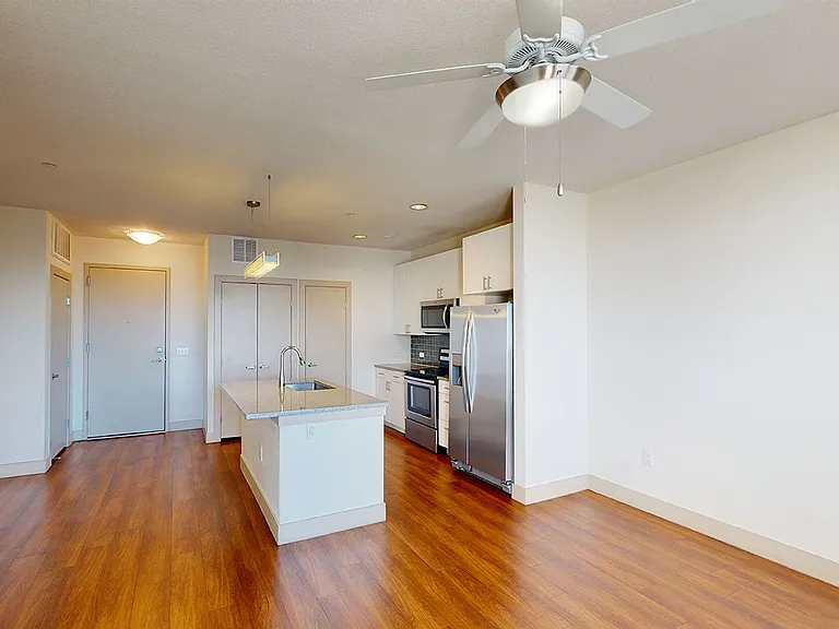 Apartment kitchen with stainless steel appliances, dining and living room with wood-style flooring.