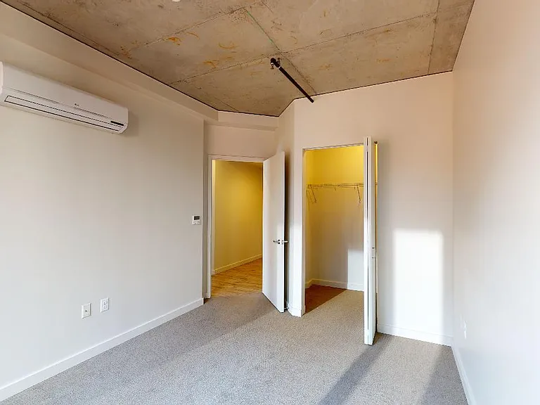 Spacious apartment bedroom with large closet and plush carpet flooring.