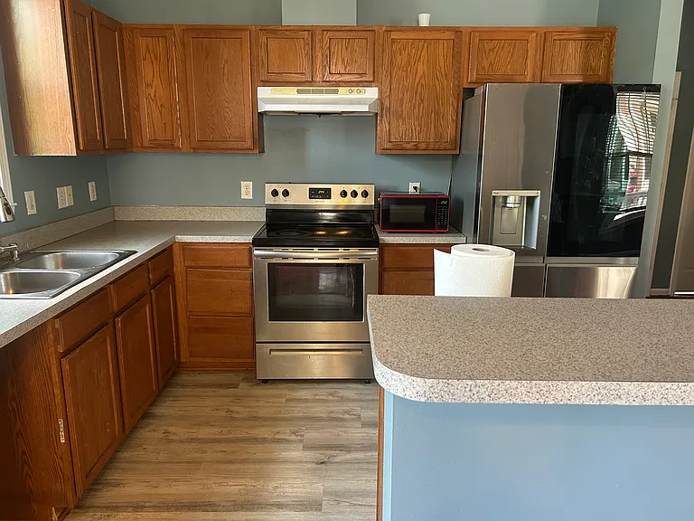 The kitchen features warm wood cabinetry and stainless steel appliances. The fridge, oven/stove, and microwave are all included, ready for your move-in.