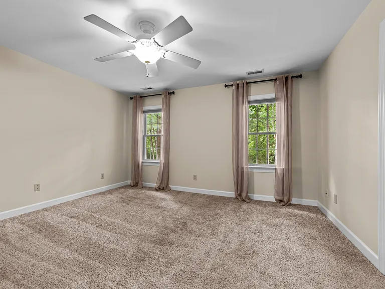 Generous primary bedroom with plush carpet, two windows, ceiling fan, and neutral finishes.