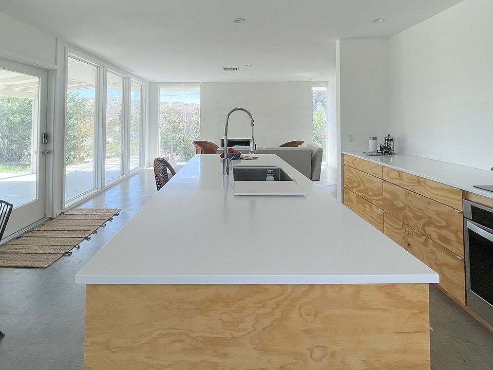 9X3 FOOT Corian covered kitchen Island is centerpiece of kitchen CONSTRUCTED OUT OF DOUGLAS FIR framed by a built in banquette to the left and living room beyond. 180 degree view of surrounding hills and mountains