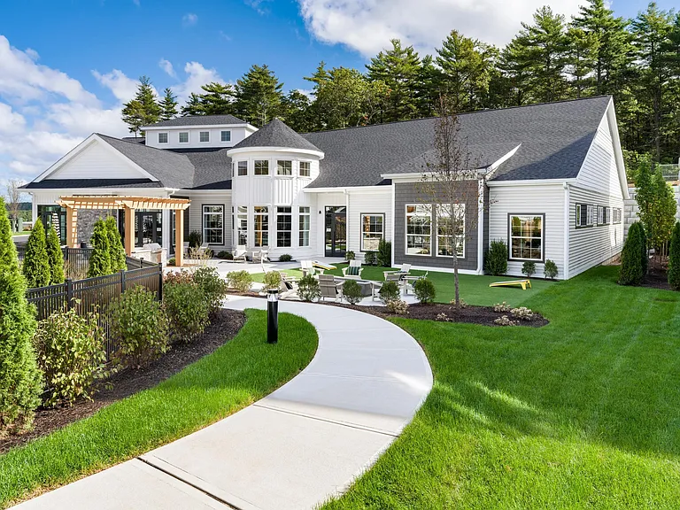 A winding walkway leads to the bright and welcoming clubhouse, complete with lounge seating, games, and inviting spaces to gather indoors and out.