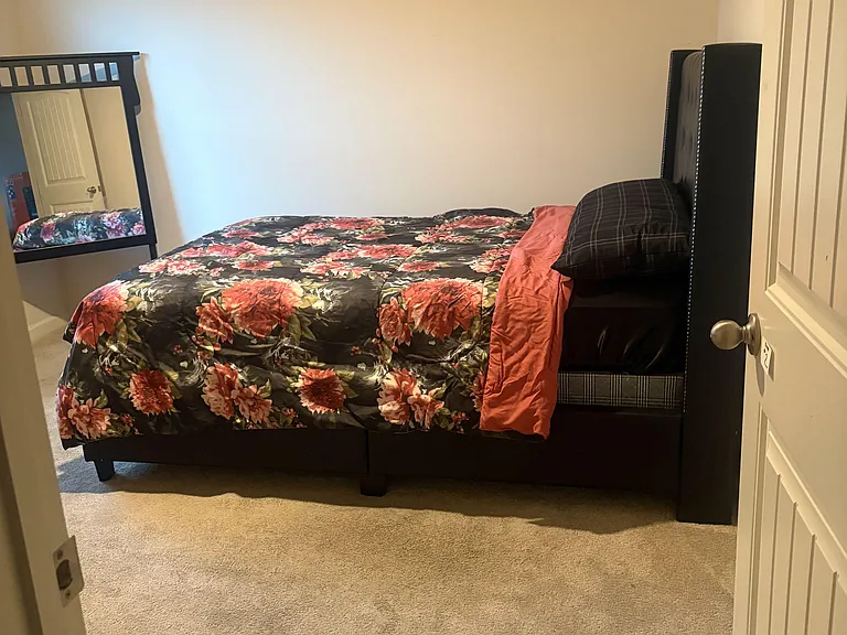 Carpeted bedroom featuring a comfortable bed setup, neutral walls, and a full-length mirror for added convenience.