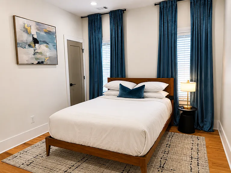 Queen bedroom with calming blackout curtains, smart TV, bedside charging, plush bedding, spacious walk-in closet, seating, and a private, restful suite-style feel.
