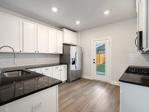 Chef-ready kitchen with black countertops, white cabinetry, and wood-style flooring.