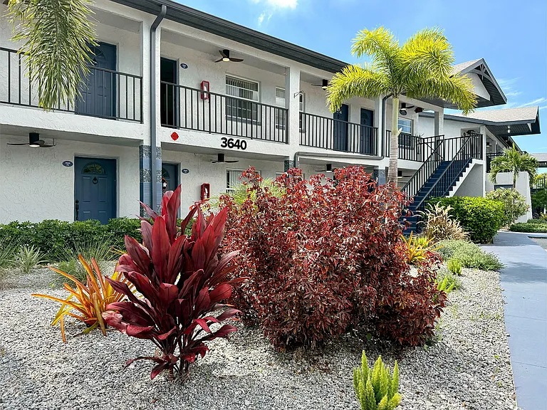 Charming apartment building with modern exterior, lush landscaping, and inviting pathway under bright blue skies.