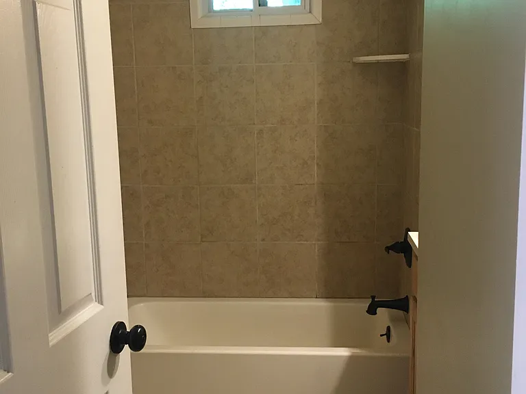 hall bathroom with tub and linen storage shelves behind bathroom door