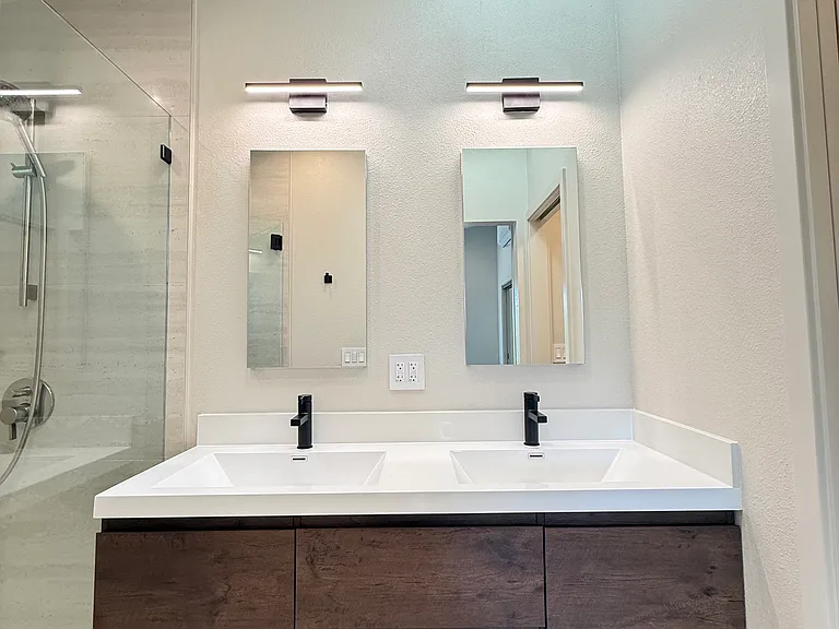 Primary suite bathroom with hanging dual vanity, large curbless stall shower with custom niche and frameless shower door.