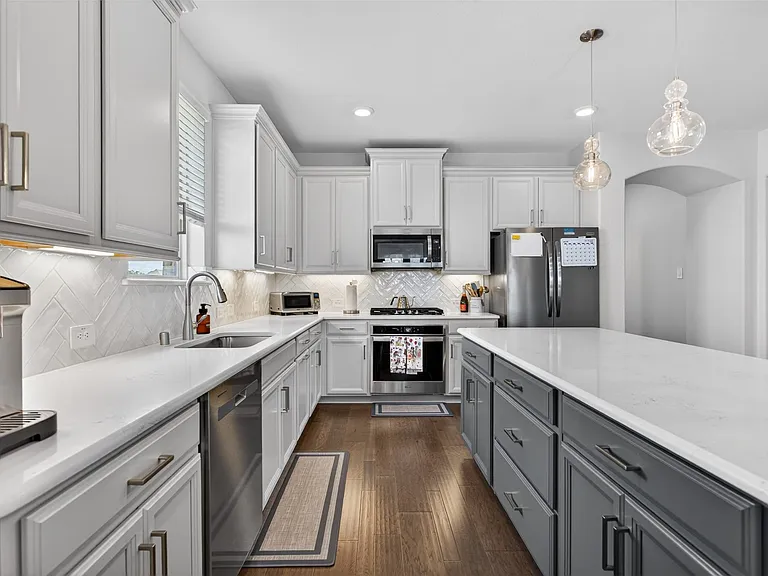 Modern kitchen featuring white upper cabinetry, dark gray lower cabinetry, and a large central island with a light-toned countertop