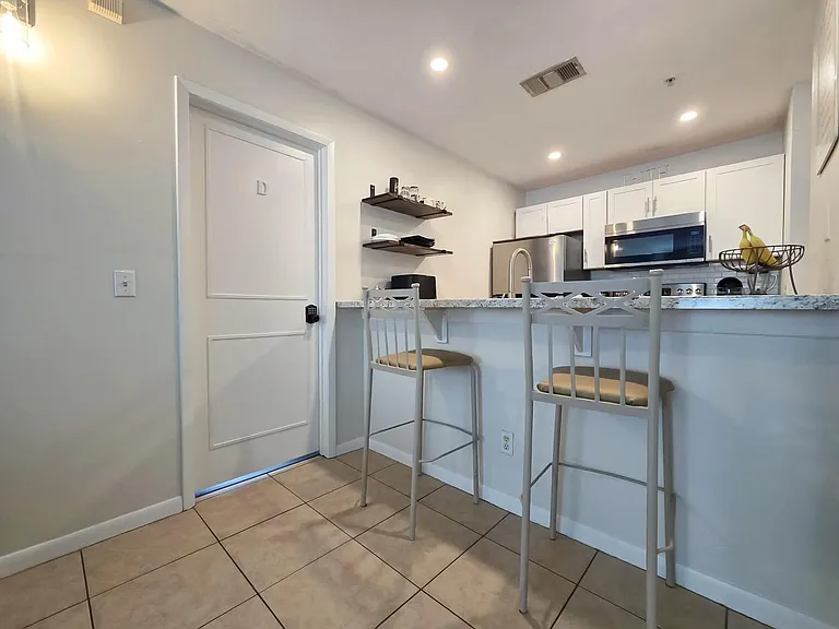 Open kitchen with breakfast bar seating, granite-style counters, and stainless steel appliances plus convenient open shelving