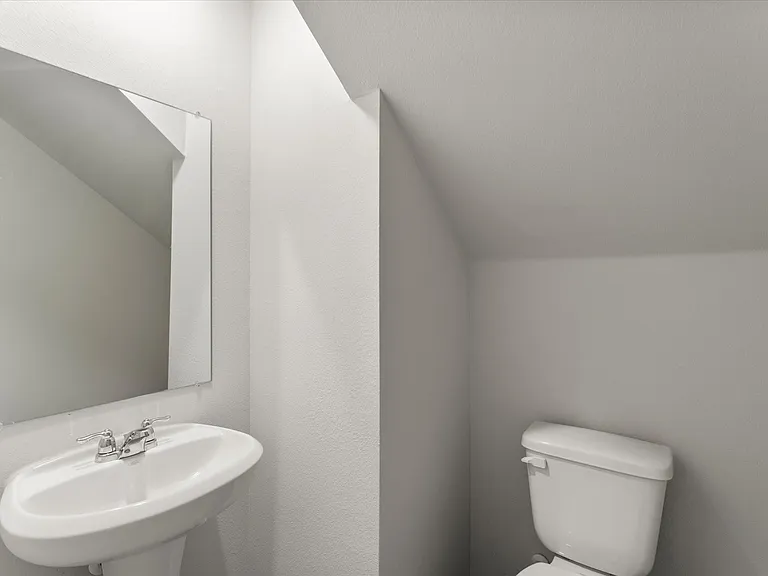 Powder room featuring a pedestal sink with chrome faucet, a frameless wall mirror, and a white toilet