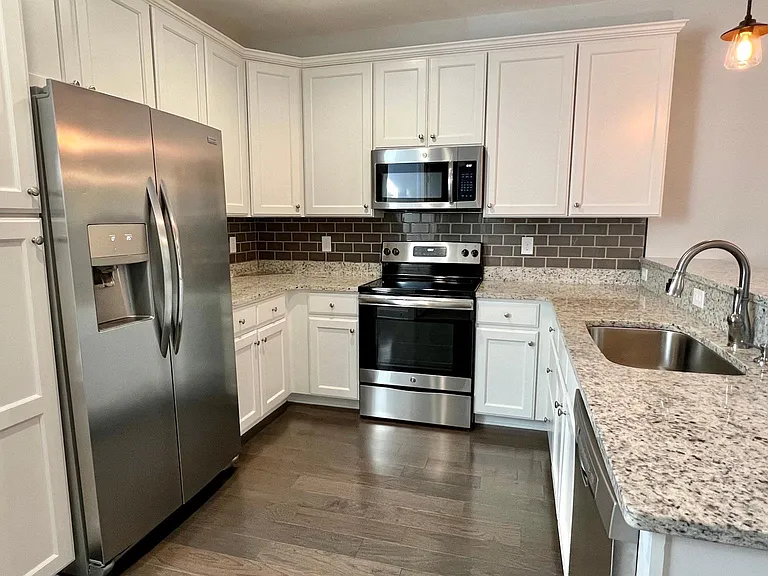 Spacious kitchen with modern white cabinets, granite counter tops, tile backsplash, stainless steel fridge, sink, oven/range, and microwave.