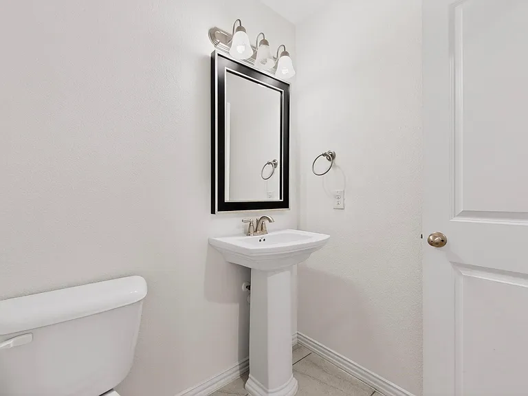 A clean and simple half-bathroom layout showcasing a sink, toilet, and a mirror on the wall.