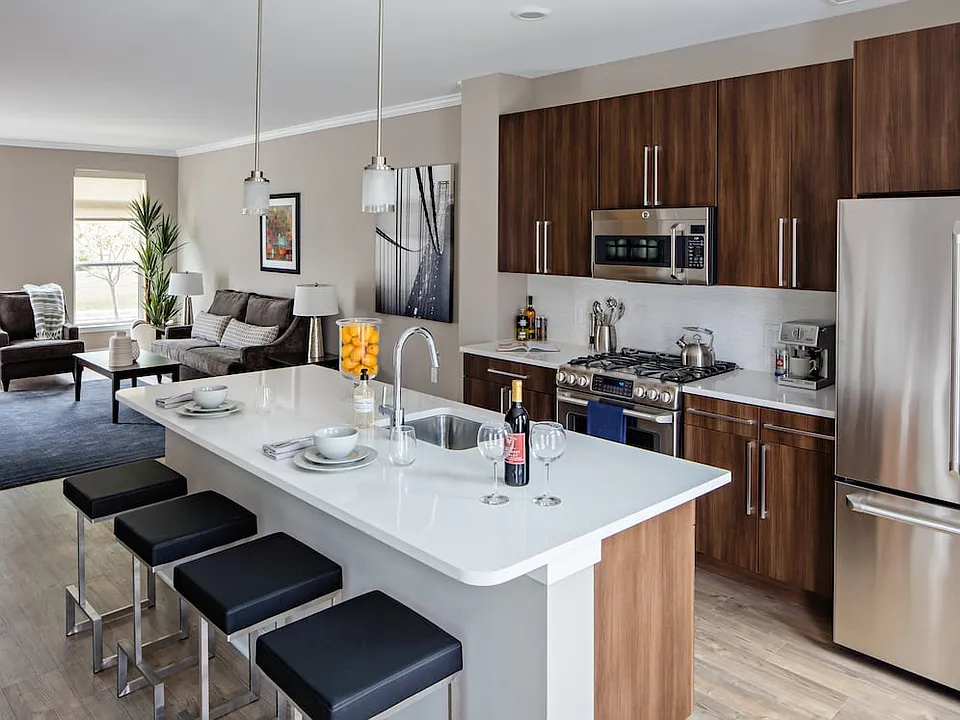 Townhome Signature Collection Kitchen with oak cabinetry, light grey quartz countertops, white tile backsplash, and hard surface flooring. Upgraded stainless steel appliances with French door refrigerator.