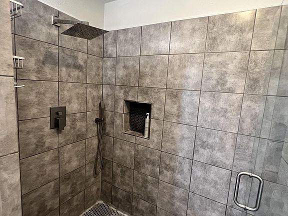 Walk-in tiled shower with rainfall showerhead, handheld sprayer, built-in niche, and pebble-style floor for easy upkeep.