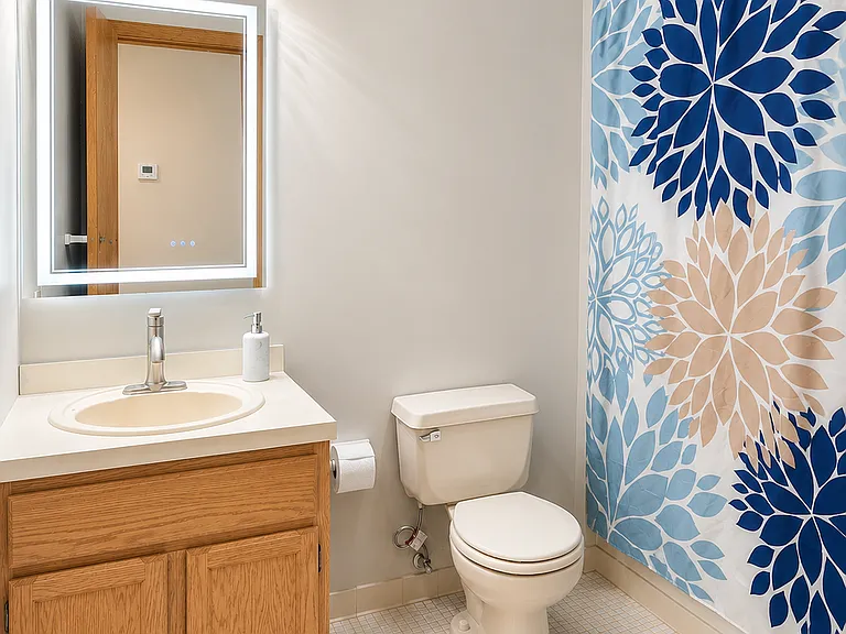 Updated full bathroom with LED mirror, modern vanity lighting, and colorful shower curtain