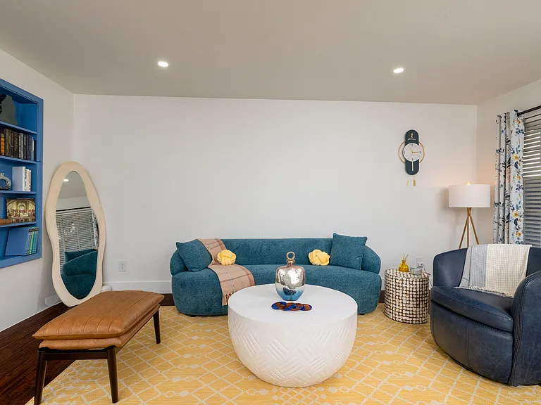 Relax in a bright and stylish living room featuring cozy blue seating, warm accents, and a modern round coffee table. Perfect for lounging, reading, or gathering with friends.