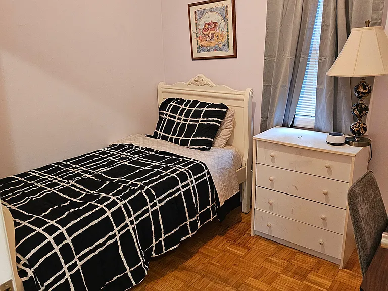 Furnished bedroom with a twin bed, dresser, and nightstand, plus a window with curtains for light and privacy.