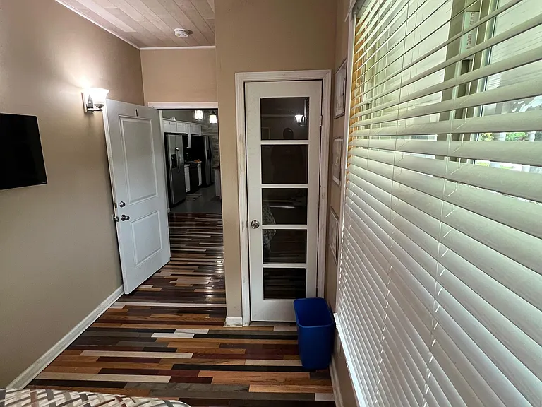 Private bedroom with wood-look flooring, a large window with blinds, and convenient access to the kitchen area.