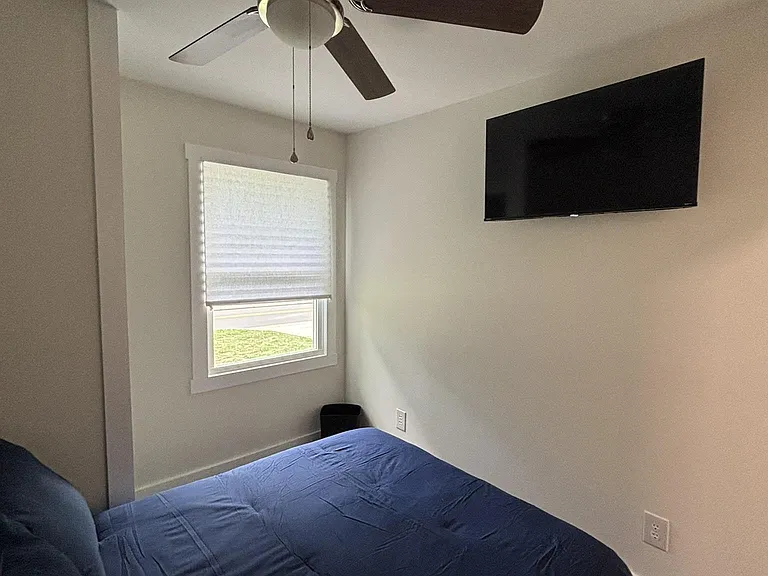 Private bedroom with ceiling fan, wall-mounted TV, and a window with blinds for comfortable everyday living.