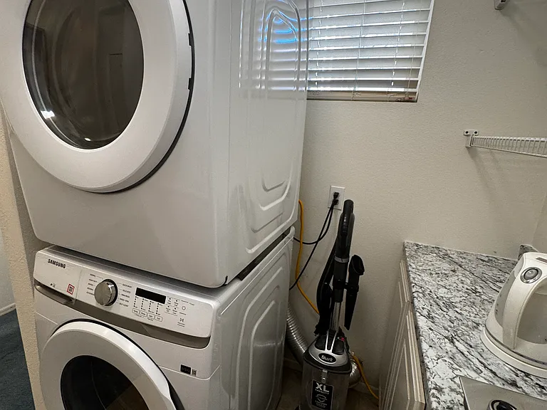 New washer/dryer set, kitchenette counter with electric kettle, cooktop, shelves, sink, trash can, vacuum