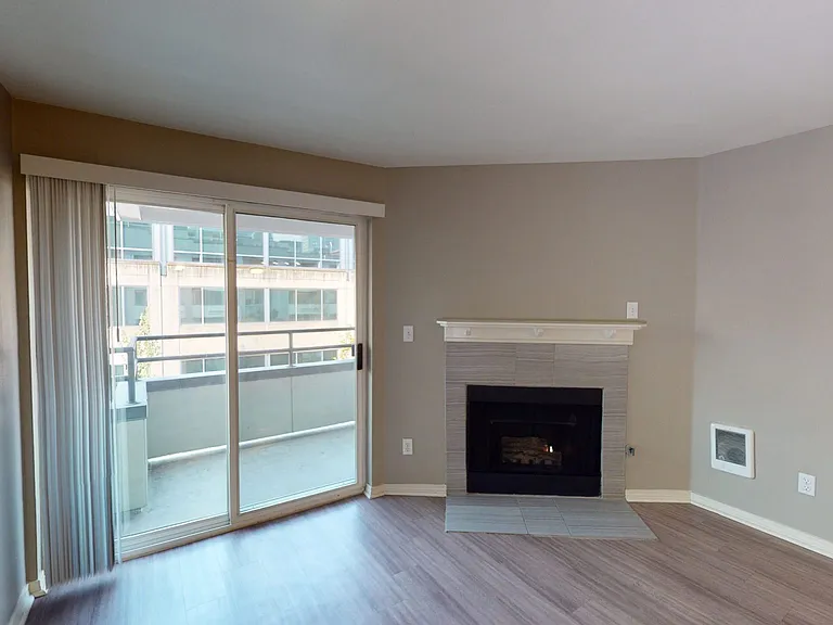 Apartment living room with wood-style flooring, fireplace and balcony in select homes.
