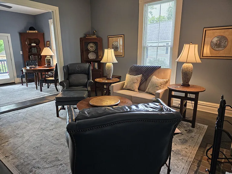 View of Keeping room and back entrance from corner of Living room. Tables fold up, can be moved to accommodate different layout/use of area. Love seat is a recliner; chairs are vintage leather.