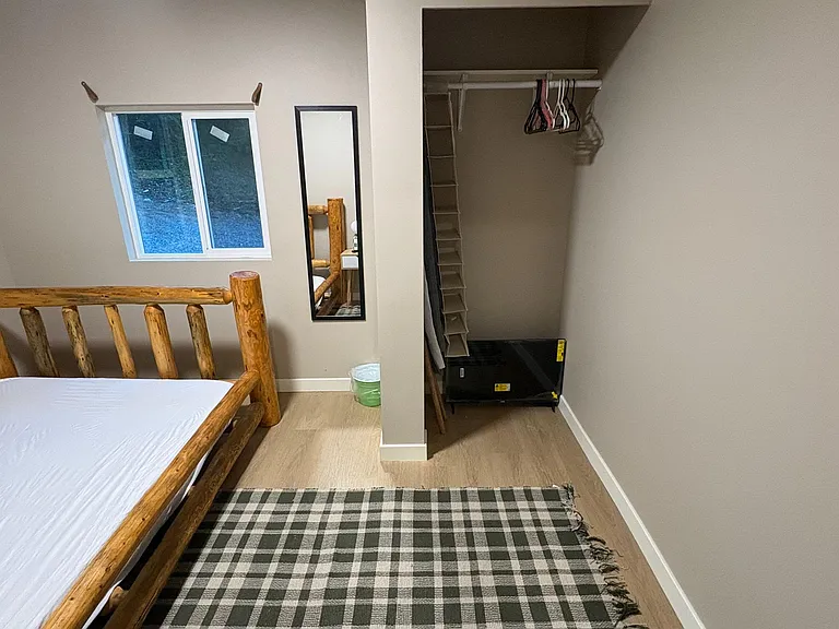 Bedroom with a large window, full-length mirror, and closet storage, plus space for a bed and small furnishings.