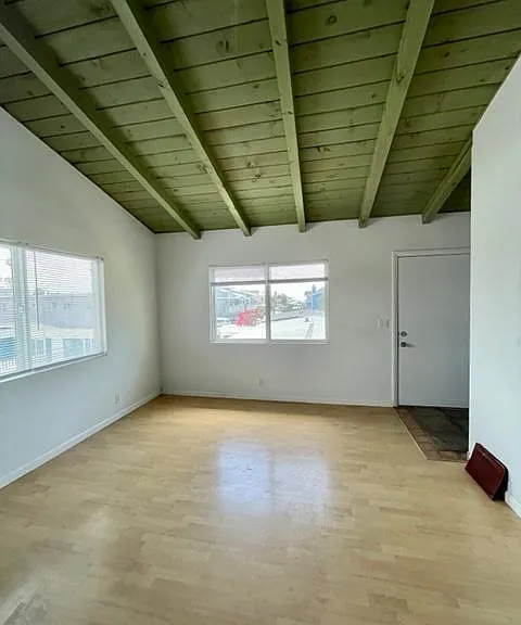 Entry door opening to great room with open beam ceiling and wood floor