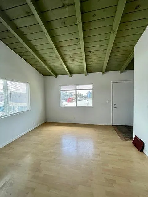 Entry door opening to great room with open beam ceiling and wood floor