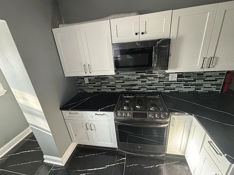 Updated kitchen with shaker cabinets, mosaic tile backsplash, and a gas range with over-the-range microwave.